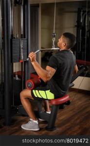 Handsome young african descent mixed race man doing lats pull-down workout in gym. Young man doing lats pull-down workout