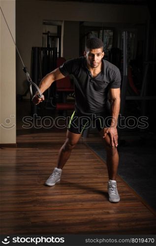 Handsome young african descent mixed race man doing one arm standing high cable fly workout in gym. Young man doing one arm standing high cable fly