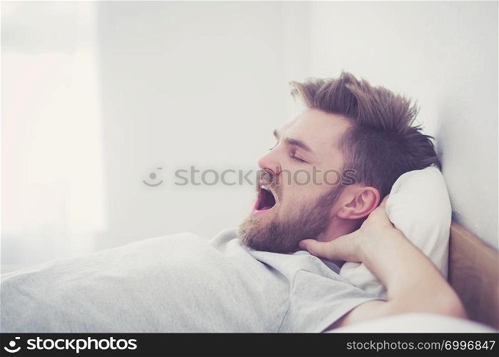 Handsome young american male yawn sleeping in bed at home - healthcare concept.