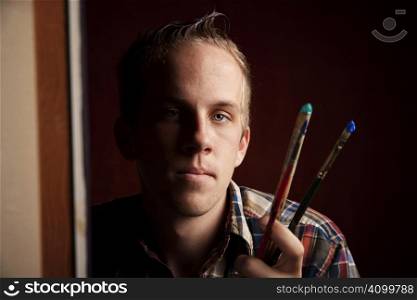 Handsome young artist holding brushes