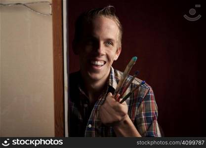 Handsome young artist holding several paint brushes