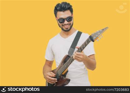 Handsome young asian men playing guitar and listen music with headphones isolated on yellow background
