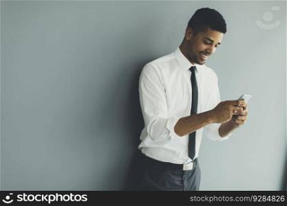 Handsome young black man with mobile phoneby grey wall  in the office