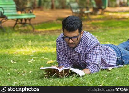 Handsome young boy reading while lying on grass in park