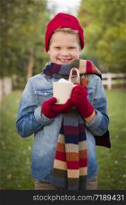 Handsome Young Boy Wearing Holiday Clothing Holding Hot Cocoa with Marshmallows and Candy Cane Outside.