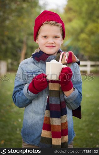 Handsome Young Boy Wearing Holiday Clothing Holding Hot Cocoa with Marshmallows and Candy Cane Outside.