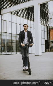 Handsome young business man in a casual clothes riding an electric scooter by an office building on a business meeting