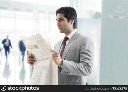 Handsome young business man looking away with newspaper in hand
