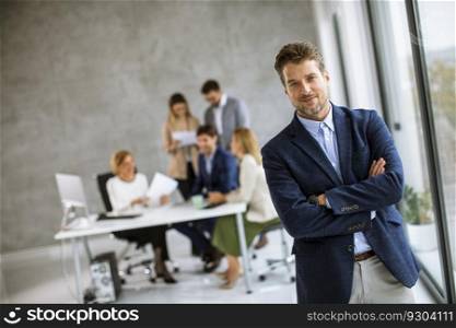 Handsome young business man standing confident in the office in front of his team