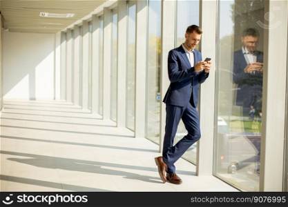 Handsome young business man using mobile phone in the modern office hallway