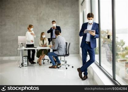 Handsome young business man wearing protective facial mask while holding digital tablet in the office space