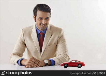 Handsome young businessman looking at toy car at office desk