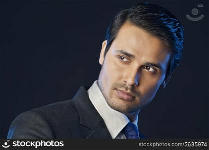 Handsome young businessman looking away over black background