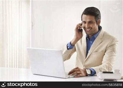 Handsome young businessman on call using laptop at office desk