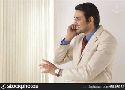 Handsome young businessman on call while looking through window blinds