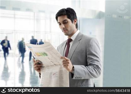 Handsome young businessman reading newspaper in office building