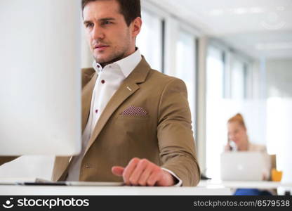 Handsome young businessman using computer in office with female colleague in background