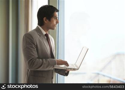 Handsome young businessman using laptop while looking outside