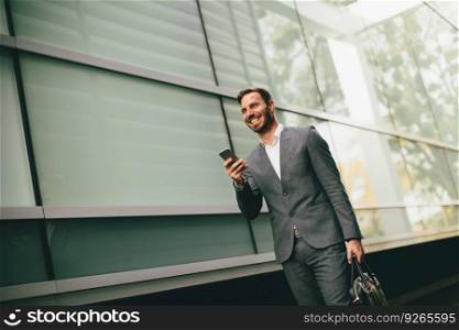 Handsome young businessman walking with mobile phone in front of office building