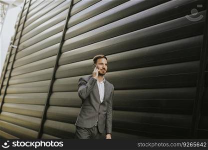 Handsome young businessman walking with mobile phone in front of office building