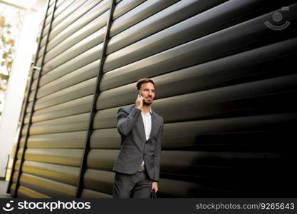 Handsome young businessman walking with mobile phone in front of office building