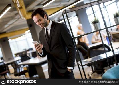 Handsome young businessman wearing black suit using modern smartphone in the office