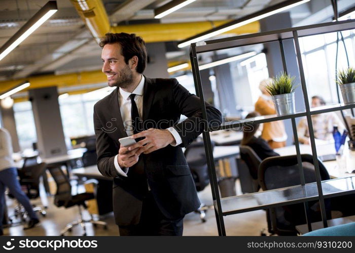 Handsome young businessman wearing black suit using modern smartphone in the office