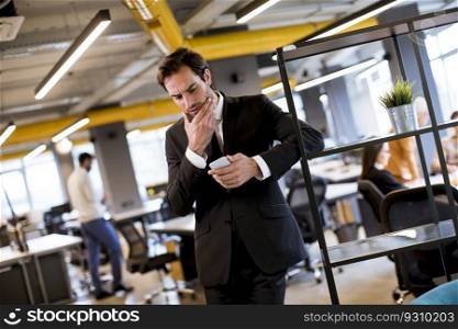 Handsome young businessman wearing black suit using modern smartphone in the office