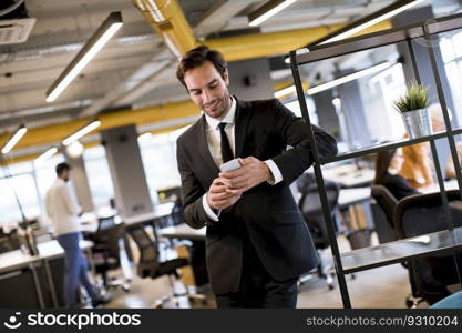 Handsome young businessman wearing black suit using modern smartphone in the office