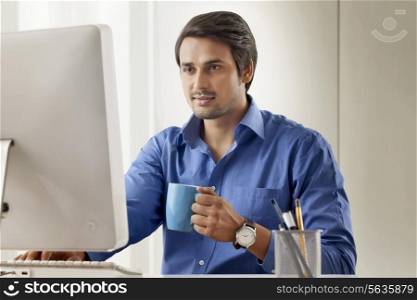 Handsome young businessman with coffee cup using computer in office