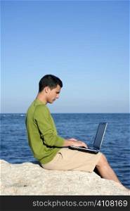 Handsome young businessman with computer on the blue ocean beach