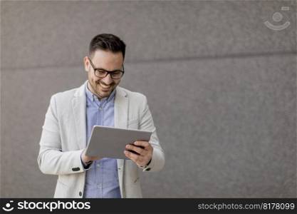 Handsome young businessman with digital tablet by the grey wall