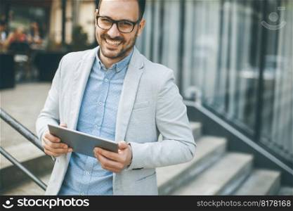 Handsome young businessman with digital tablet by the office building