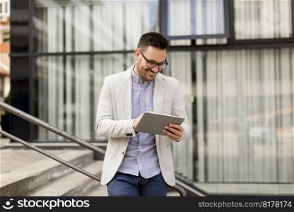Handsome young businessman with digital tablet by the office building