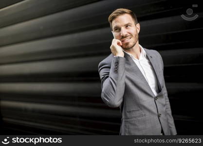 Handsome young businessman with mobile phone by office building