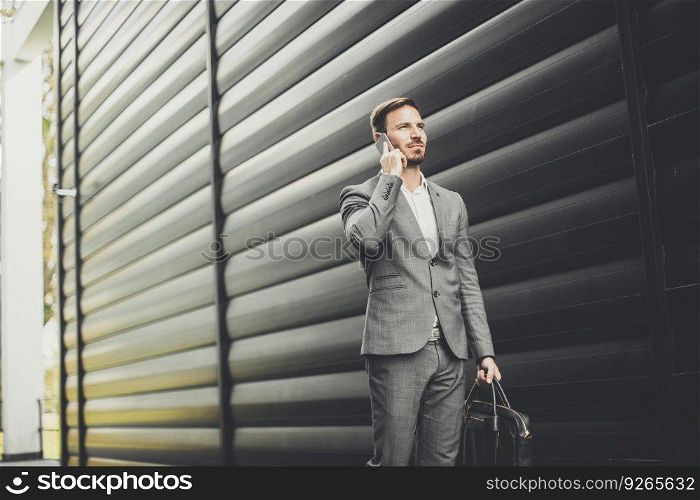 Handsome young businessman with mobile phone by office building