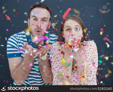 handsome young couple celebrating new year and chrismas party while blowing confetti decorations to camera isolated over gray background