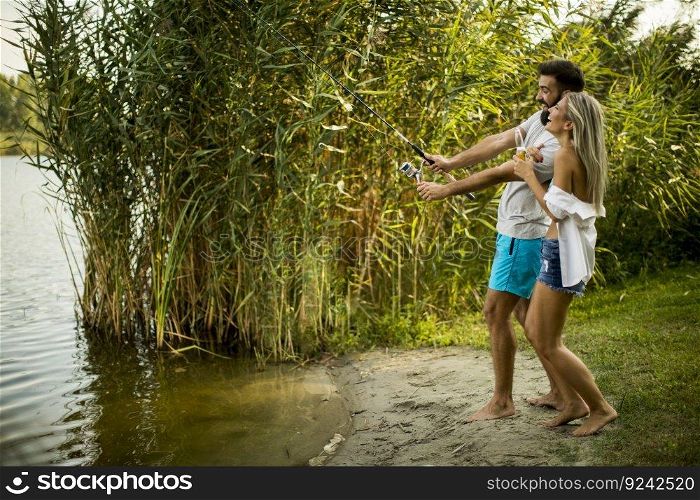 Handsome young couple enjoying fishing on lake at sunny summer day