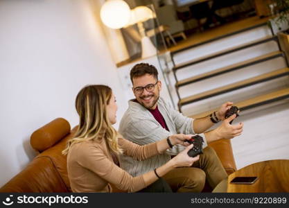 Handsome young couple playing video games at home, sitting on sofa and enjoying themselves