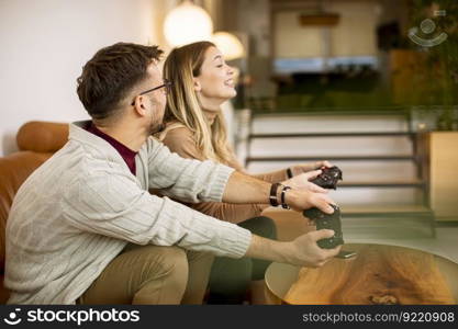 Handsome young couple playing video games at home, sitting on sofa and enjoying themselves