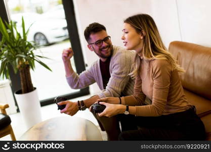 Handsome young couple playing video games at home, sitting on sofa and enjoying themselves