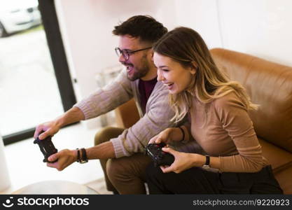 Handsome young couple playing video games at home, sitting on sofa and enjoying themselves