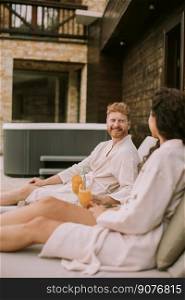 Handsome young couple relaxing on beds and drinking fresh orange juice on the outdoor terrace