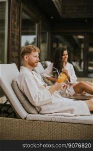 Handsome young couple relaxing on beds and drinking fresh orange juice on the outdoor terrace