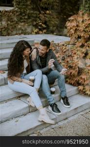 Handsome young couple sitting on outdoor stairs on a autumn day and using mobile phone
