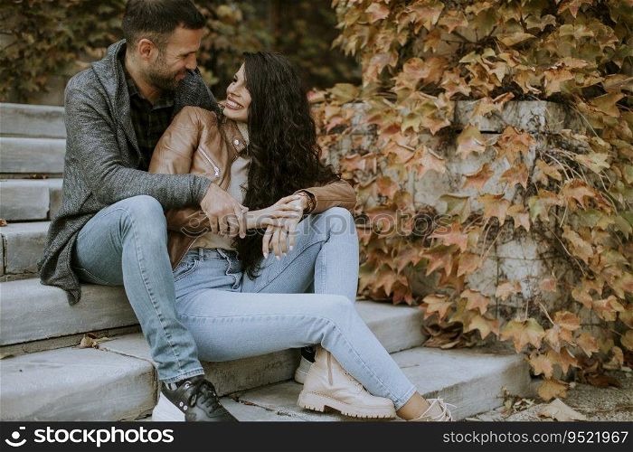 Handsome young couple sitting on outdoor stairs on a autumn day and using mobile phone