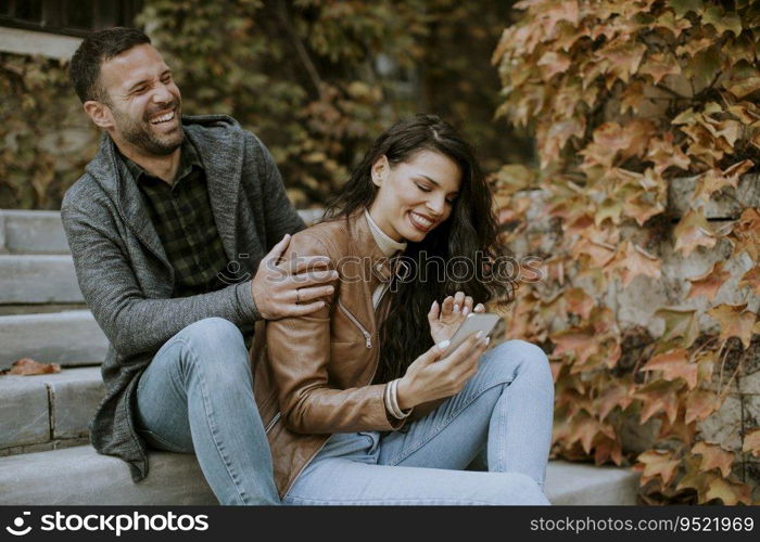 Handsome young couple sitting on outdoor stairs on a autumn day and using mobile phone