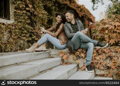 Handsome young couple sitting with mobile phones on outdoor stairs on a autumn day
