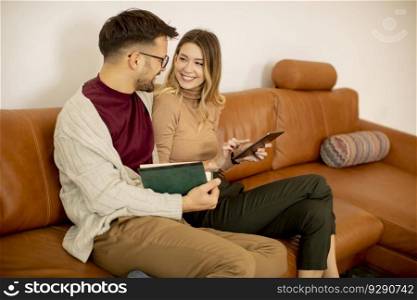 Handsome young couple using digital tablet together while sitting on sofa at home