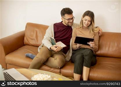 Handsome young couple using digital tablet together while sitting on sofa at home